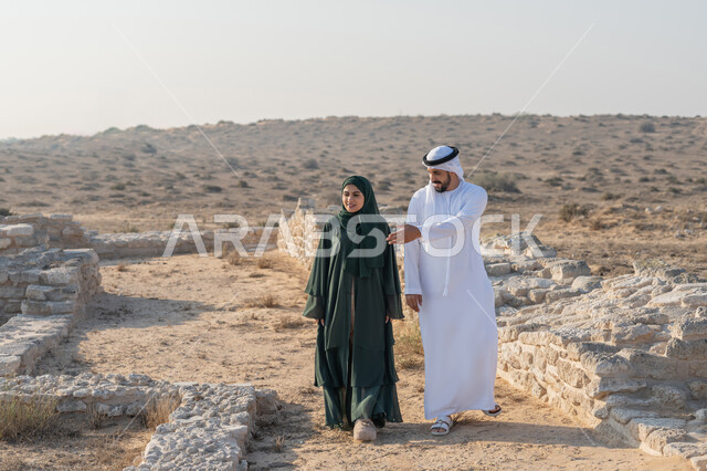اليوم الوطني الاماراتي 1971، تأسيس الاتحاد 2 ديسمبر، شاب عربي خليجي إماراتي يرتدي الكندورة والغترة يتجول مع إمراة ترتدي العباءة والحجاب في منطقة أثرية في الصحراء، تعابير وايماءات الفخر والاعتزاز وحب الوطن، تبادل الاحاديث وزيارة الاماكن التاريخية القديمة
