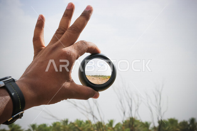 صورة مقربة ليد رجل يحمل بيده عدسة عالية الدقة ، هواية تصوير الاماكن الطبيعية ، صور خلابة للطبيعة ، مصور محترف ، دقة التصوير