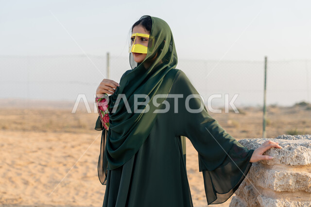 ذكرى تأسيس الاتحاد 2 ديسمبر، الاحتفال باليوم الوطني الاماراتي 1971، إمراة عربية خليجية إماراتية ترتدي الحجاب والعباءة والبرقع الذهبي تقف في منطقة اثرية تاريخية في الصحراء وقت النهار، حب الوطن والانتماء اليه، تعابير وايماءات الفخر والاعتزاز
