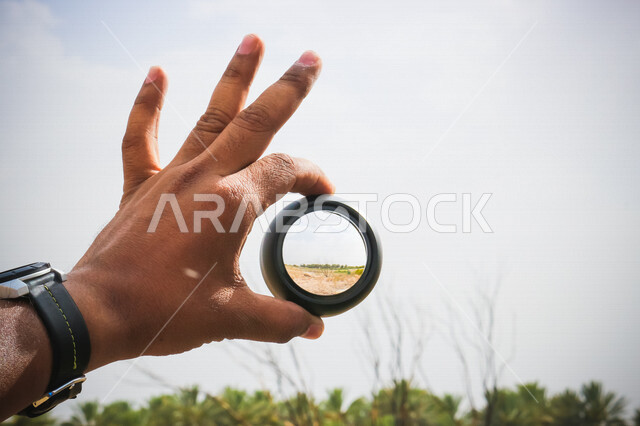 صورة مقربة ليد رجل يحمل بيده عدسة عالية الدقة ، هواية تصوير الاماكن الطبيعية ، صور خلابة للطبيعة ، مصور محترف ، دقة التصوير