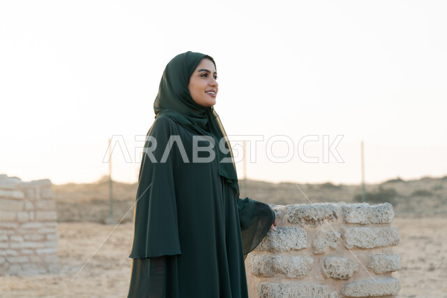 Founding of the Union December 2, Celebrating the UAE National Day 1971, An Arab Gulf Emirati woman wearing a hijab and abaya stands in a historical archaeological area in the desert during the day, love of the homeland and belonging to it, expressions and gestures of pride and honor
