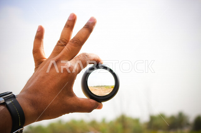 صورة مقربة ليد رجل يحمل بيده عدسة عالية الدقة ، هواية تصوير الاماكن الطبيعية ، صور خلابة للطبيعة ، مصور محترف ، دقة التصوير