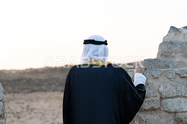 زيارة الاماكن التاريخية القديمة، اليوم الوطني الاماراتي 1971، الاحتفال بذكرى تأسيس الاتحاد 2 ديسمبر، صورة من الخلف لرجل عربي خليجي إماراتي يرتدي الكندورة والبشت مع الغترة يقف في منطقة أثرية في الصحراء، حب الوطن والانتماء اليه، تعابير الفخر والاعتزاز، خلفية الطبيعة