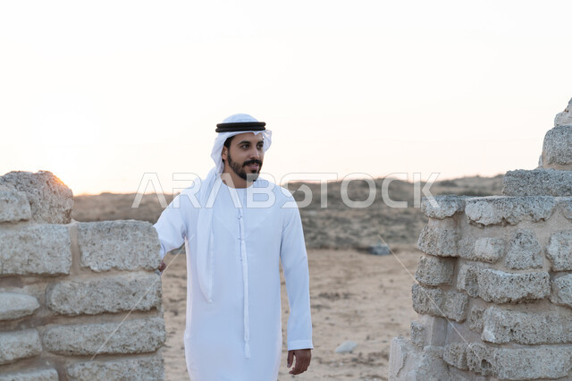 اليوم الوطني الاماراتي 1971، زيارة الاماكن التاريخية القديمة، الاحتفال بذكرى تأسيس الاتحاد 2 ديسمبر، شاب عربي خليجي إماراتي يرتدي الكندورة والغترة البيضاء يقف في منطقة أثرية في الصحراء، حب الوطن والانتماء اليه، تعابير وايماءات الفخر والاعتزاز، خلفية الطبيعة الصحراوية