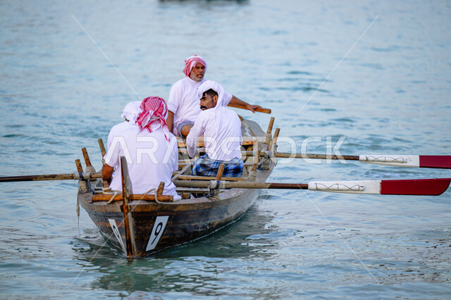 الاستمتاع بالرحلة البحرية, ممارسة هواية الصيد، رجال عرب خليجيون قطريون يرتدون الثوب التقليدي يبحرون في قارب خشبي على شاطئ مدينة الدوحة، مهرجان كتارا الرابع عشر للمحامل التقليدية, نشاط ترفيهي ممتع, فعاليات وأنشطة تراثية وثقافية