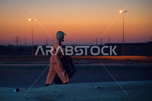 صورة لعامل النظافة يرتدي الزي الخاص بالعمل ، يهتم بنظافة شوارع المدينة في الصباح الباكر ، جمال المملكة العربية السعودية ، منظر شروق الشمس في الصباح الباكر