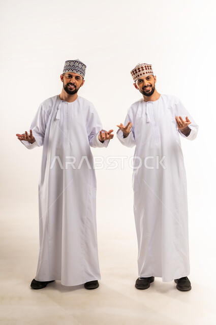 الاستفهام والاستفسار عن شيء ما، ايماءات عدم المعرفة والدهشة والاستغراب, بورتريه لشابين توأم عربيين خليجيين عمانيين يرتديان الدشداشة والكمة يرفعان يديهما بتعابير التساؤل, الجسم بالطول الكامل, خلفية بيضاء