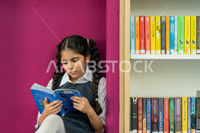 الاهتمام بتصفح الكتب المفيدة، تنمية مهارة المطالعة للطلاب, حب الثقافة والاستطلاع، طالبة عربية خليجية إماراتية ترتدي الزي المدرسي تقوم بقراءة كتاب بإيماءات التركيز، قضاء وقت الفراغ بالتعلم والتثقف الذاتي, زيارة مكتبة المدرسة، التعليم والدراسة في الإمارات