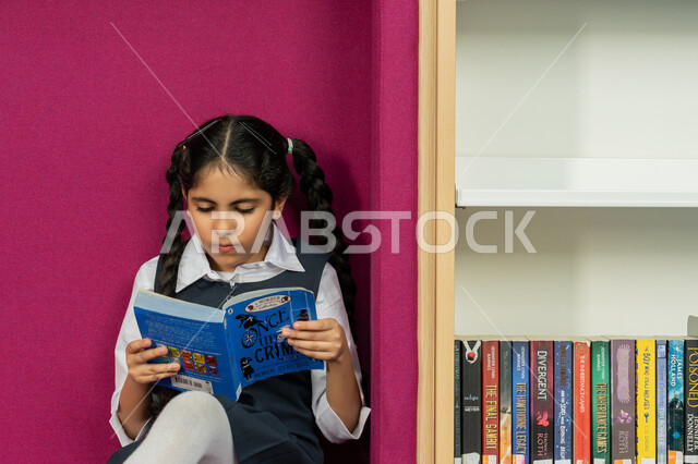 قضاء وقت الفراغ بالتعلم والتثقف الذاتي, زيارة مكتبة المدرسة، الاهتمام بتصفح الكتب المفيدة، تنمية مهارة المطالعة للطلاب, حب الثقافة والاستطلاع، طالبة عربية خليجية إماراتية ترتدي الزي المدرسي تقوم بقراءة كتاب بإيماءات التركيز، التعليم والدراسة في الإمارات