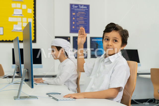 استخدام جهاز تقني حديث في التعلم، المنهاج المتطور والتعليم الالكتروني في المدرسة، المشاركة الفعالة للتلاميذ، إيماءات الحماس لمعرفة الجواب الصحيح، طالب عربي خليجي إماراتي يرتدي الزي المدرسي يرفع يده للإجابة عن السؤال، التفاعل والنشاط داخل الفصل الدراسي