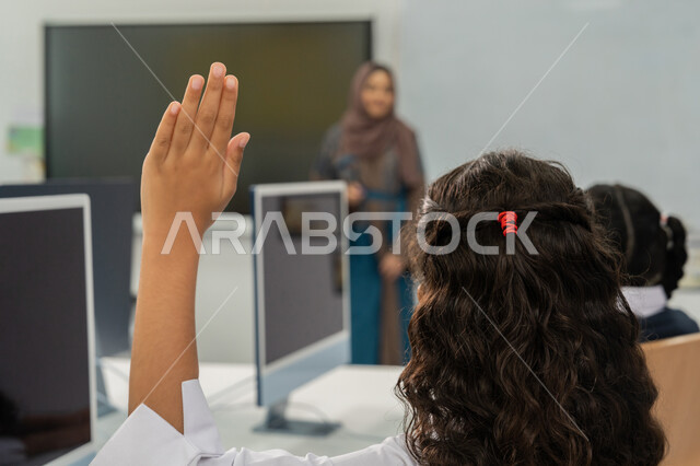استخدام جهاز تقني حديث في التعلم، المشاركة الفعالة للتلاميذ، التعليم الالكتروني في المدرسة، طالبة ترفع يدها للإجابة عن السؤال، معلمة عربية خليجية إماراتية ترتدي الحجاب والعباءة تقف أمام سبورة مدرسية بيضاء، النشاط داخل الفصل الدراسي، تطور طريقة التدريس في الإمارات