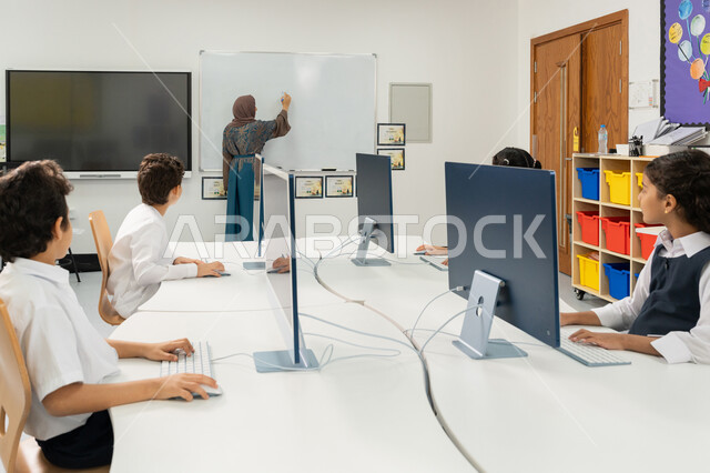تطور طريقة التدريس في مدارس الإمارات العربية المتحدة، المنهاج المتطور والتعليم الالكتروني في المدرسة، معلمة عربية خليجية إماراتية ترتدي الحجاب والعباءة تقوم بشرح الدرس على لوحة مدرسية بيضاء، استخدام جهاز تقني حديث في التعلم والدراسة داخل الفصل الدراسي