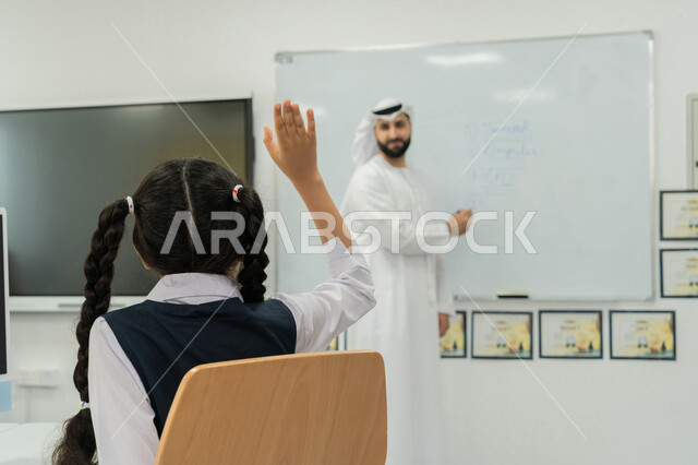 استخدام جهاز تقني حديث في التعلم، تطور طريقة التدريس في مدارس الإمارات، طالبة إماراتية ترفع يدها للإجابة على السؤال، التعليم الالكتروني في المدرسة، معلم عربي خليجي إماراتي يرتدي الكندورة والغترة يشرح الدرس على سبورة مدرسية بيضاء، التفاعل والنشاط داخل الفصل الدراسي