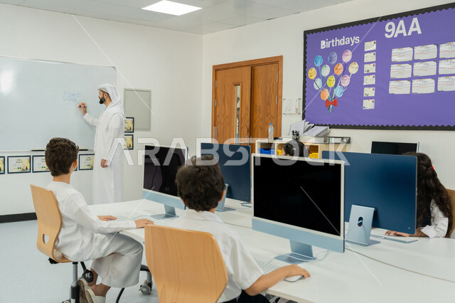 استخدام جهاز تقني حديث في التعلم والدراسة داخل الفصل الدراسي، المنهاج المتطور والتعليم الالكتروني في المدرسة، معلم عربي خليجي إماراتي يرتدي الكندورة والغترة يقوم بشرح الدرس على لوحة مدرسية بيضاء، تطور طريقة التدريس في مدارس الإمارات العربية المتحدة