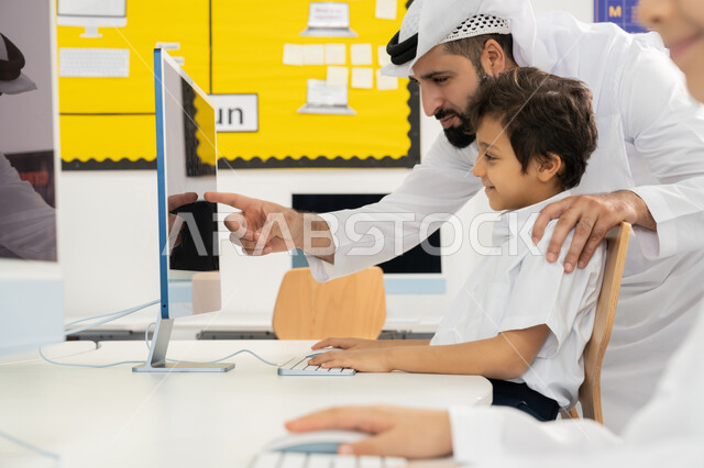 Quality of effective learning methods, advanced curriculum and e-learning in school, use of modern technical device in classroom study, development of teaching method in UAE schools, Emirati Gulf Arab teacher wearing kandura explaining lesson to student using computer