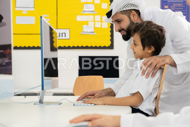 Quality of effective learning methods, advanced curriculum and e-learning in school, use of modern technical device in classroom study, development of teaching method in UAE schools, Emirati Gulf Arab teacher wearing kandura explaining lesson to student using computer