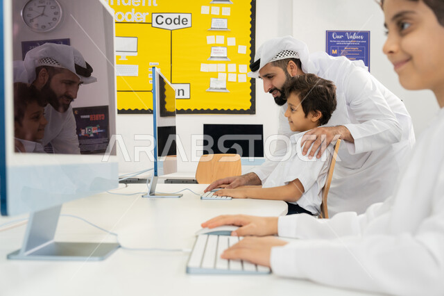 تطور طريقة التدريس في مدارس الامارات العربية المتحدة، معلم عربي خليجي اماراتي يرتدي الكندورة يقوم بشرح الدرس للطالب باستخدام الحاسوب، جودة أساليب التعلم الفعال، المنهاج المتطور والتعليم الالكتروني في المدرسة، استخدام جهاز تقني حديث في الدراسة داخل الفصل الدراسي