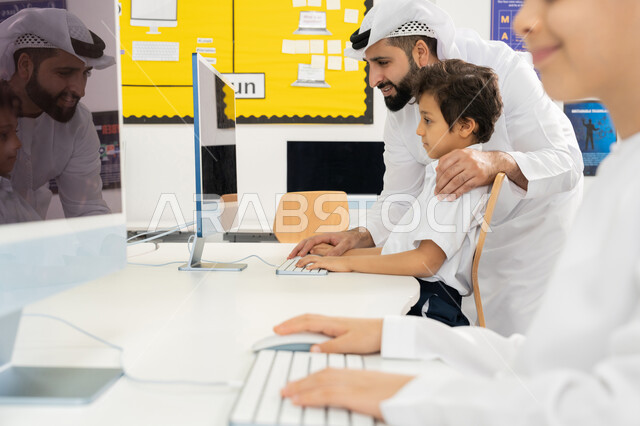 جودة أساليب التعلم الفعال، المنهاج المتطور والتعليم الالكتروني في المدرسة، استخدام جهاز تقني حديث في الدراسة داخل الفصل الدراسي، تطور طريقة التدريس في مدارس الامارات العربية المتحدة، معلم عربي خليجي اماراتي يرتدي الكندورة يقوم بشرح الدرس للطالب باستخدام الحاسوب
