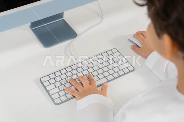 Typing on a keyboard, the development of teaching methods in UAE schools, a close-up image from the back of an Emirati Gulf Arab student wearing a kandura studying using a computer, the advanced curriculum and e-learning in school, the use of a modern technical device in learning and studying inside the classroom