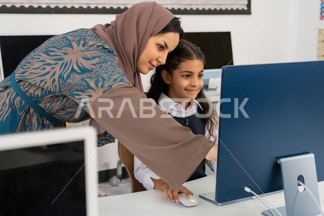 استخدام جهاز تقني حديث  في التعلم والدراسة داخل الفصل الدراسي، تطور طريقة التدريس في مدارس الامارات العربية المتحدة، معلمة عربية خليجية اماراتية محجبة ترتدي العباءة تقوم بشرح الدرس للطالبة باستخدام الحاسوب، المنهاج المتطور والتعليم الالكتروني في المدرسة