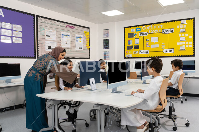 تطور طريقة التدريس في مدارس الامارات العربية المتحدة، معلمة عربية خليجية اماراتية محجبة ترتدي العباءة تقوم بشرح الدرس للطلاب باستخدام الحاسوب، المنهاج المتطور والتعليم الالكتروني في المدرسة، استخدام جهاز تقني حديث في التعلم والدراسة داخل الفصل الدراسي