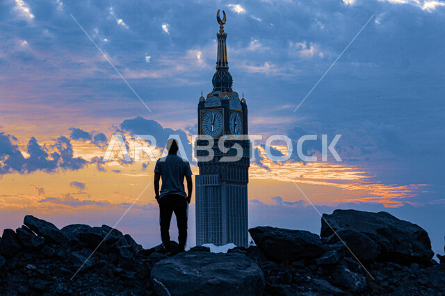 An aesthetic image at sunset and sunrise of a man standing in front of the clock tower from the top of Mount Al-Khandaqah, Makkah Al-Mukarramah, the beauty and splendor of the Kingdom of Saudi Arabia