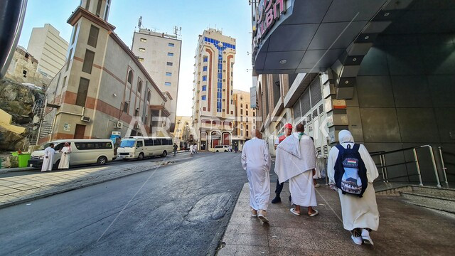 معالم دينية اسلامية مقدسة، مجموعة من الحجاج والمعتمرين يرتدون ملابس الاحرام يسيرون على طريق المشاة في مكة المكرمة، النمو والتقدم العمراني للأبراج وناطحات السحاب، الفن الهندسي المعماري على الطراز الحديث في المملكة العربية السعودية