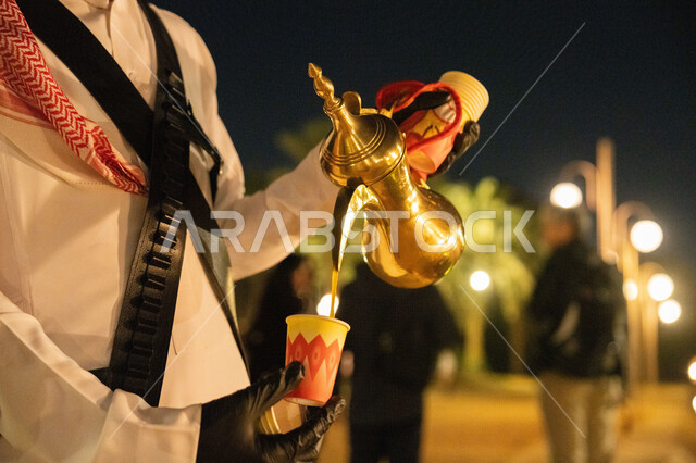 التمسك بالقيم  المتوارثة من الأجداد، مفهوم كرم الضيافة وحسن الإستقبال، العادات والتقاليد الأصيلة, صورة مقربة لايدي رجل عربي خليجي سعودي يرتدي الشماغ والثوب التقليدي يمسك بيده دلة قهوة عربية، الاستمتاع بالمشروبات الساخن