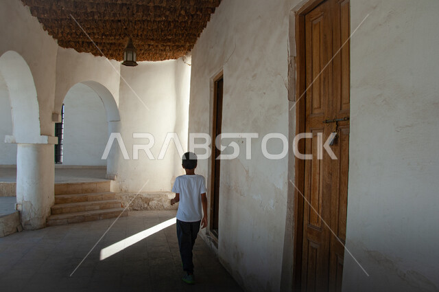 قدوم الزوار والسائحين، الفن الهندسي المعماري على الطراز التقليدي الأثري في المنطقة الشرقية، المعالم التراثية الدينية في المملكة العربية السعودية، صورة من الخلف لولد عربي خليجي امام الأبواب الخشبية المزخرفة في قصر إبراهيم التاريخي في محافظة الأحساء في الهفوف