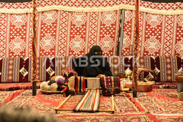صناعة تقليدية شعبية، غزل الانسجة والقماش، حرفة صنع المشالح في المملكة العربية السعودية، سيدة عربية خليجية سعودية محجبة ترتدي النقاب تقوم بحياكة الخيوط، الفن التراثي الحرفي التقليدي