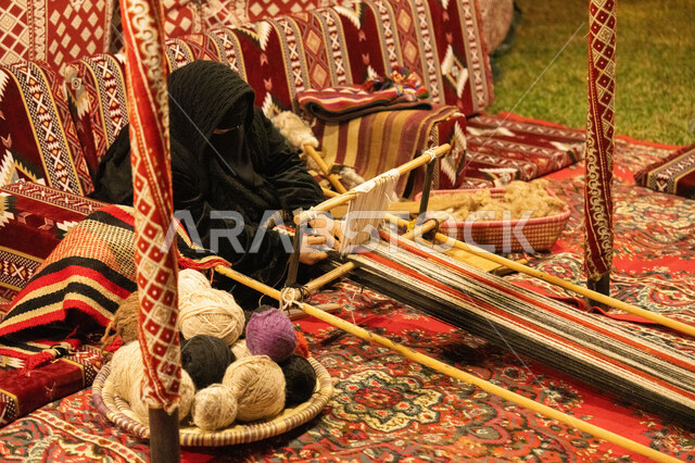 غزل الانسجة والقماش، صناعة تقليدية شعبية، حرفة صناعة المشالح في المملكة العربية السعودية، سيدة عربية خليجية سعودية محجبة ترتدي النقاب تقوم بحياكة الخيوط، الفن التراثي الحرفي التقليدي