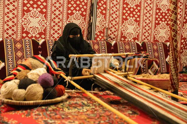 غزل الانسجة والقماش، صناعة تقليدية شعبية، حرفة صناعة المشالح في المملكة العربية السعودية، سيدة عربية خليجية سعودية محجبة ترتدي النقاب تقوم بحياكة الخيوط، الفن التراثي الحرفي التقليدي