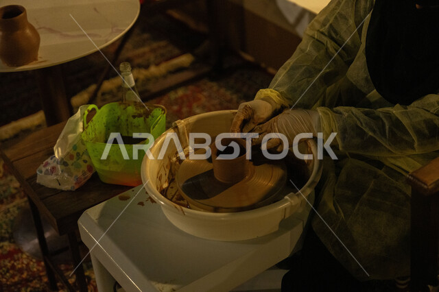 العمل في صناعة الخزفيات, حرفة وصناعة يدوية شعبية من التراث السعودي العريق، آنية خزفية مصنوعة من الطين، الجرار الفخارية المزخرفة، صورة مقربة لايدي امرأة عربية سعودية خليجية تقوم بصناعة الفخار