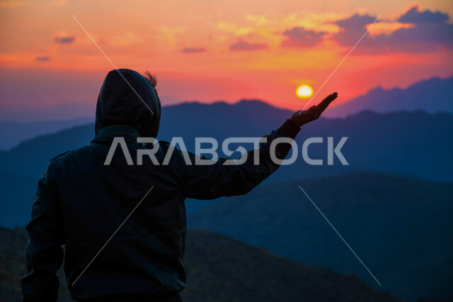 صورة ظلية لرجل عربي خليجي سعودي يستمتع بالطبيعة الخلابة و منظر الغروب على جبال منطقة بني سعد في مدينة الطائف ، روعة و جمال الطبيعة الخلابة في المملكة العربية السعودية