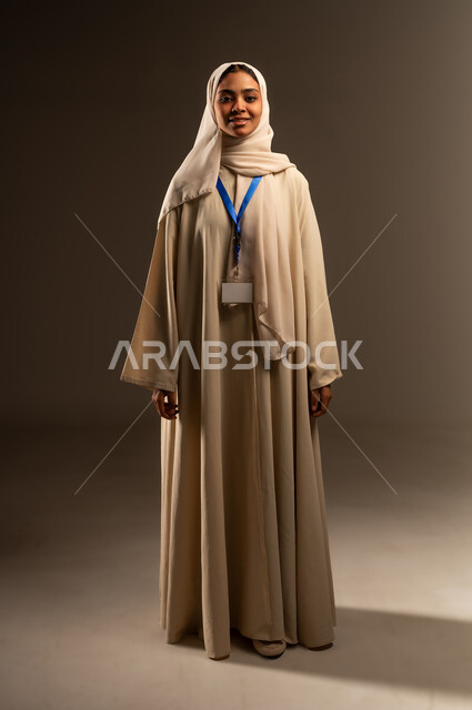 إبراز الهوية الشخصية، بطاقه تعريفية وهوية، التعبير عن الذات، موك اب ابيض، بورتريه لإمرأه عربيه خليجية سعودية محجبة مبتسمه ترتدي العباءة تقف باستقامة تنظر الى الكاميرا بإيماءات الثقة بالنفس، صورة الجسم بالطول الكامل، خلفية رمادية