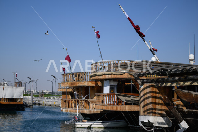 مرسى السفن الشراعية على كورنيش مدينة الدوحة في النهار, مناطق الرحلات والجولات البحرية الترفيهية, المعالم والأماكن السياحية الساحلية المشهورة, أعلام دولة قطر ترفرف في السماء