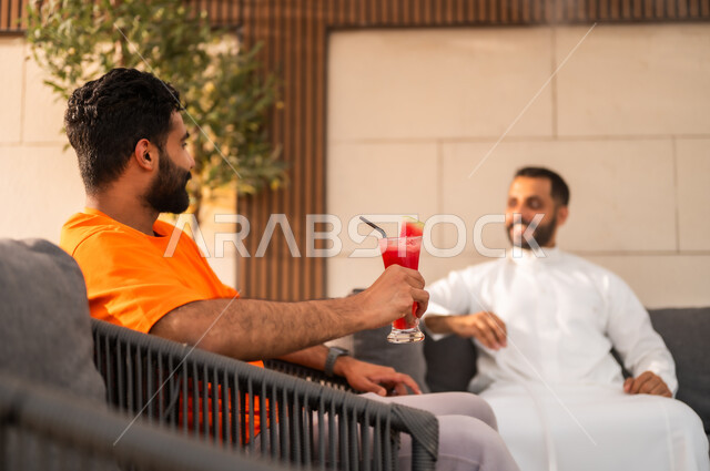 الأجواء الشبابية في الكافيهات السعودية، شابان عربيان خليجيان سعوديان يجلسان معا في احد المطاعم ويتبادلان أطراف الحديث، قضاء أوقات ممتعة في الويكند، الترويح عن النفس والخروج في سهرات مسائية للقاء الأصدقاء، تناول العصائر الباردة ومشروبات السموذي الموسمية المنعشة