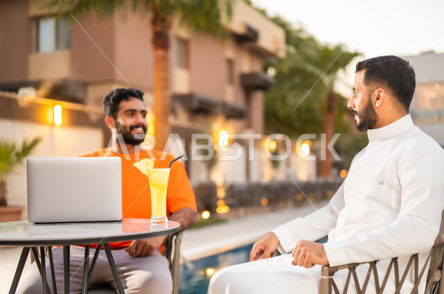 الأجواء الشبابية في الكافيهات السعودية، شابان عربيان خليجيان سعوديان يجلسان معا في احد المطاعم ويتبادلان أطراف الحديث، قضاء أوقات ممتعة في الويكند، الترويح عن النفس والخروج في سهرات مسائية للقاء الأصدقاء، تناول العصائر الباردة ومشروبات السموذي الموسمية المنعشة
