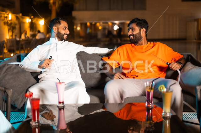 قضاء أوقات ممتعة في الويكند، تناول العصائر الباردة المنعشة وتدخين الشيشة، الأجواء الشبابية في الكافيهات السعودية، شابان عربيان خليجيان سعوديان يجلسان معا في احد المطاعم ويتبادلان أطراف الحديث، الترويح عن النفس والخروج في سهرات مسائية للقاء الأصدقاء