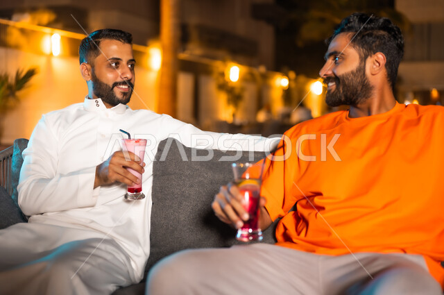 الأجواء الشبابية في الكافيهات السعودية، شابان عربيان خليجيان سعوديان يجلسان معا في احد المطاعم ويتبادلان أطراف الحديث، قضاء أوقات ممتعة في الويكند، الترويح عن النفس والخروج في سهرات مسائية للقاء الأصدقاء، تناول العصائر الباردة ومشروبات السموذي الموسمية المنعشة