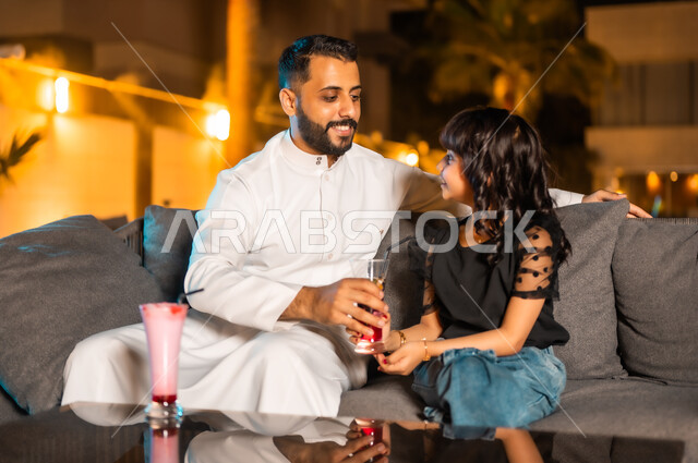 تقوية روابط المودة والحب بين الأب وابنته، القيام بنشاطات ممتعة بعطلة نهاية الأسبوع، أجواء صيفية لطيفة في المطاعم والمقاهي بالمملكة العربية السعودية، رجل عربي خليجي سعودي يرتدي الثوب التقليدي برفقة ابنته يجلسان في المطعم ويتناولان العصائر الباردة المنعشة