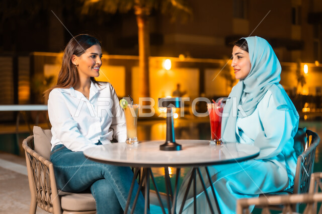 اجتماع الصديقات والقيام بنشاطات ممتعة بعطلة نهاية الأسبوع، ارتياد المطاعم والمقاهي في المملكة العربية السعودية، جلسة وناسة وتسلية في أجواء صيفية لطيفة، صديقتان عربيتان خليجيتان سعوديتان تجلسان أمام المسبح في الهواء الطلق،  مناقشة ومشاركة الأحاديث وآخر الأخبار