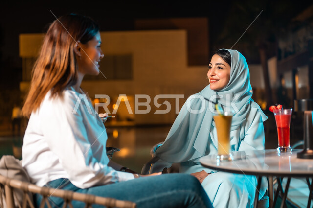 A fun and entertaining session in a nice summer atmosphere, two Saudi Arabian Gulf friends sitting in front of the outdoor pool, visiting restaurants and cafes in the Kingdom of Saudi Arabia, friends meeting and doing fun activities on the weekend, discussing and sharing conversations and the latest news