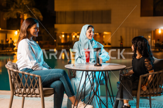 Restaurants and cafes in Saudi Arabia, friends meeting and doing fun activities on the weekend, a fun and entertaining session in a nice summer atmosphere, a veiled Saudi Gulf Arab woman wearing a colorful abaya with her little daughter and her friend sitting in a restaurant in the open air