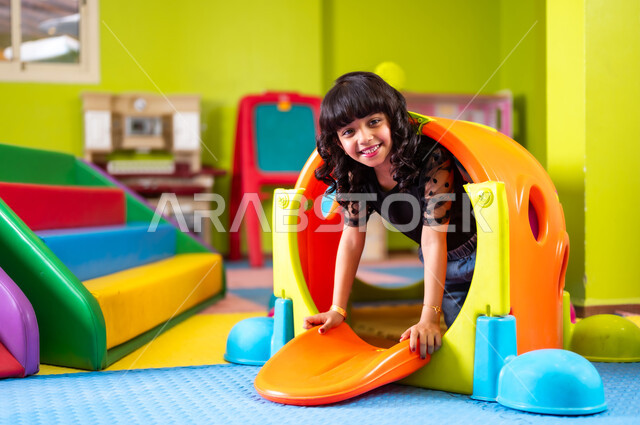 ارتياد الصالة المغلقة المخصصة للأطفال، القيام بنشاط ترفيهي في عطلة نهاية الأسبوع، فتاة صغيرة عربية خليجية سعودية ترتدي الزي الكاجوال تلهو وتلعب بحماس ونشاط، النظر إلى الكاميرا بإيماءات السعادة والسرور، تفريغ الطاقة باللعب واللهو والمرح