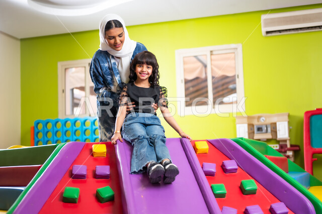 تعزيز رابط الأمومة بين الأم وابنتها، اصطحاب الأطفال إلى الصالات المخصصة للعب، مشاركة الأبناء لحظات المرح والمتعة، القيام بنشاطات عائلية في عطلة نهاية الأسبوع، فتاة عربية خليجية سعودية ترتدي الزي الكاجوال تتزحلق بمساعدة والدتها بإيماءات السعادة والسرور