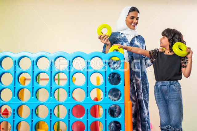 القيام بنشاط عائلي في عطلة نهاية الأسبوع، تنمية قدرات الأولاد العقلية عن طريق الألعاب الفكرية والحسية، اصطحاب الأبناء إلى صالة اللعب المخصصة للأطفال، قضاء اوقات ترفيهية ممتعة، فتاة عربية خليجية سعودية ترتدي الزي الكاجوال برفقة والدتها تلعبان سويا