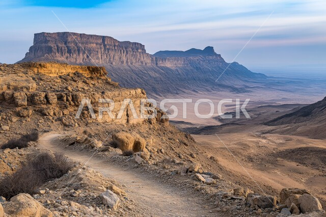 Terrain and sand dunes, rock and stone formations in the desert of the Kingdom, rock formations and rugged slopes, landscape in a valley in Saudi Arabia, harsh and dry climate in the vast deserts, high mountain peaks and heights, clear blue sky background
