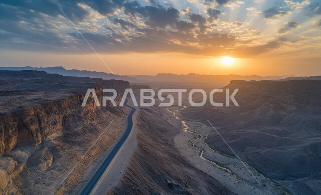 سلاسل الجبال والقمم والمرتفعات، الطرقات الجبلية الوعرة والمتعرجة, طريق اسفلتي معبد على سفح جبلي أعلى المنحدر، التضاريس والتشكلات الصخرية في صحاري المملكة، تسهيل سير السيارات والسفر والتنقل من مكان لآخر بين المدن، خلفية السماء عند الغروب