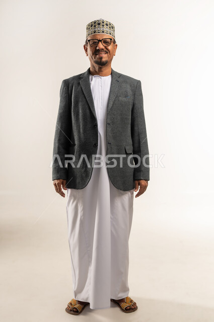 Standing up straight with self-confident expression, taking care of one's appearance, portrait of an Arab Gulf Omani man wearing a dishdasha, a turban and a winter coat, looking at the camera with gestures of pleasure and cheerfulness, wearing warm winter clothes, full body, white background